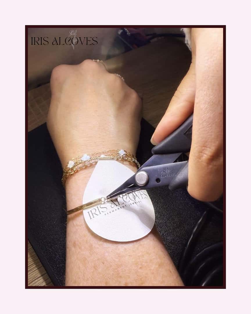 Hand wearing multiple bracelets and a white guard, as pliers connect a permanent bracelet onto the wrist.