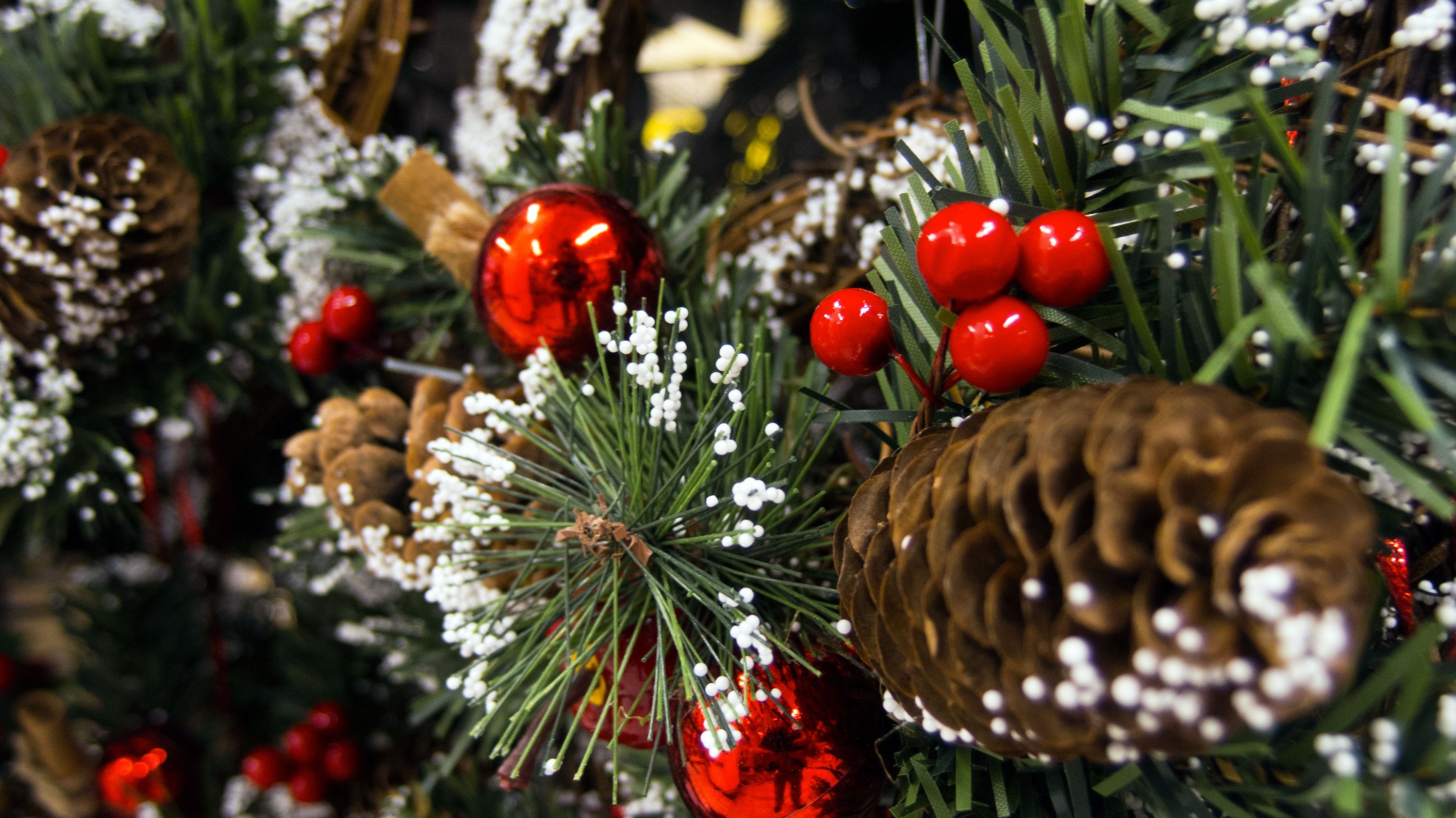 Christmas garland with green pine needles, frosted pinecones, red ornaments, and berries.