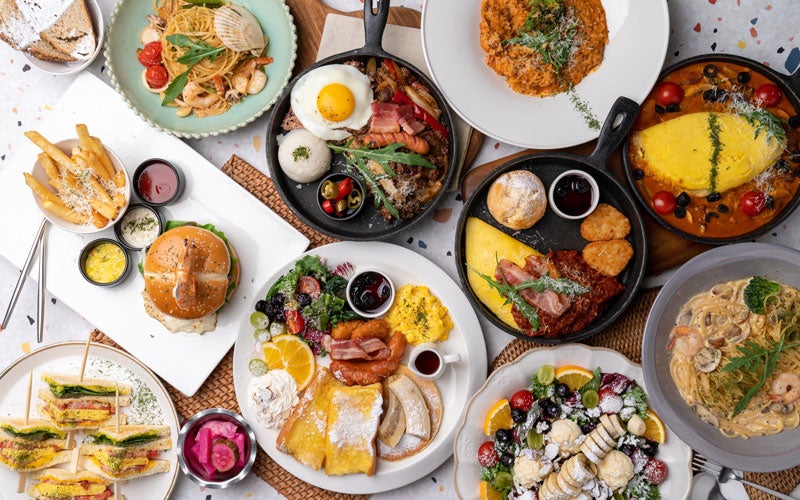An overhead shot of a table covered with a large variety of breakfast and brunch dishes, including pasta, burgers, and eggs.